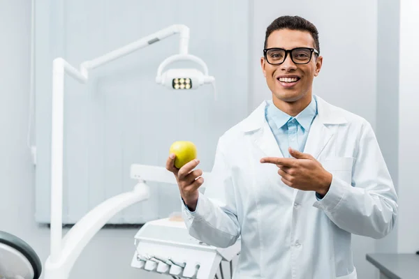 Handsome african american doctor in glasses pointing at apple — Stock Photo