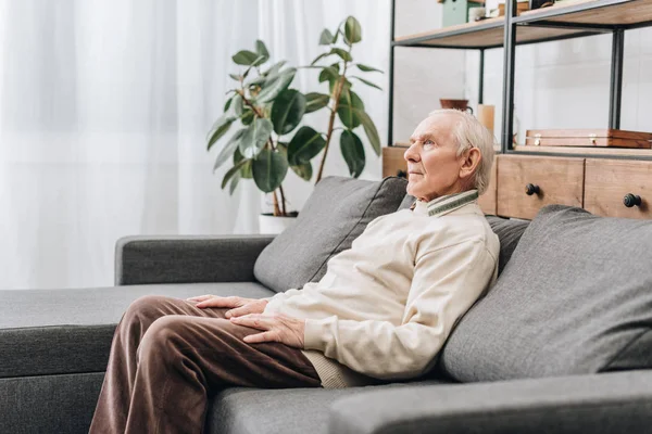 Пенсионер с седыми волосами сидит на диване — стоковое фото