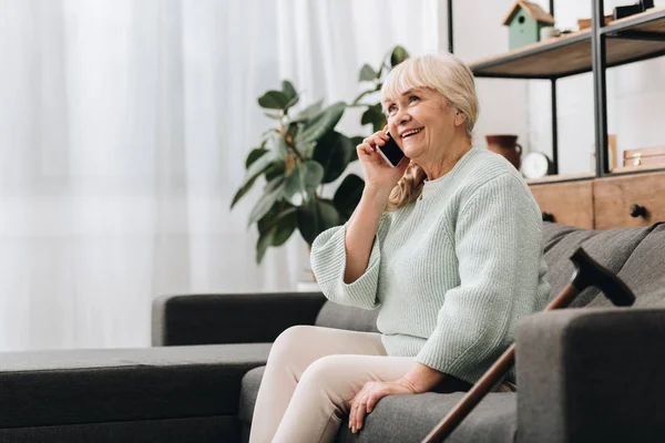 Sorrindo mulher sênior falando no smartphone enquanto sentado no sofá — Fotografia de Stock