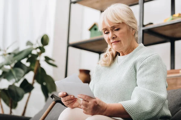 Sad retired woman holding photos in living room — Stock Photo