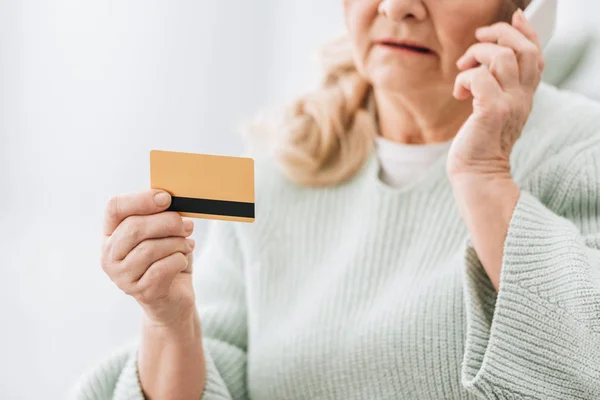 Enfoque selectivo de la tarjeta de crédito en la mano de la mujer mayor hablando en el teléfono inteligente - foto de stock