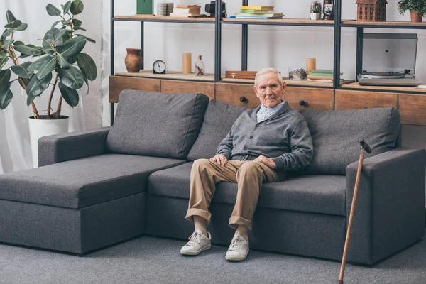 Старший мужчина с седыми волосами сидит на диване в гостиной — стоковое фото