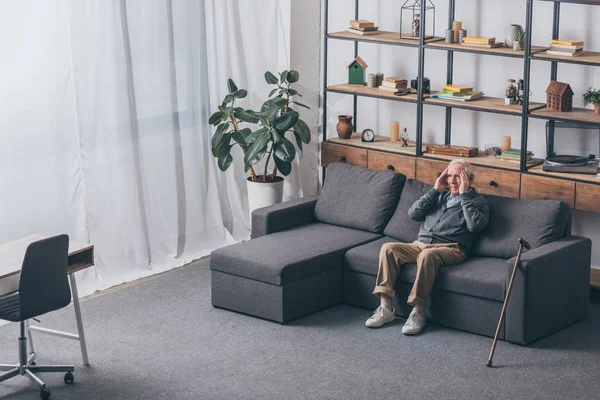 Senior man with grey hair having headache while sitting on sofa — Stock Photo