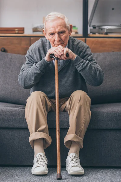 Upset retired man with grey hair holding walking cane in living room — Stock Photo