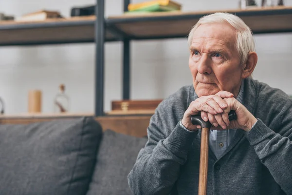 Sad retired man with grey hair holding walking cane in living room — Stock Photo