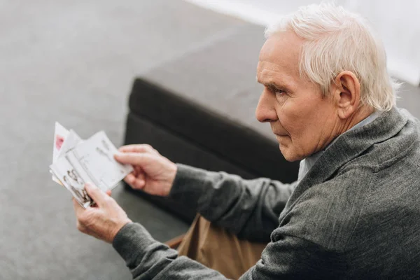 Печальный пенсионер с седыми волосами смотрит на старые фото дома — стоковое фото