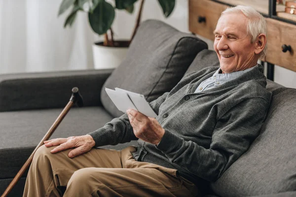 Щасливий пенсіонер з сірим волоссям дивиться на фотографії і сидить на дивані — стокове фото