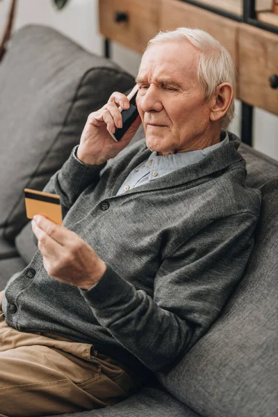 Senior spricht auf Smartphone und schaut auf Kreditkarte — Stockfoto