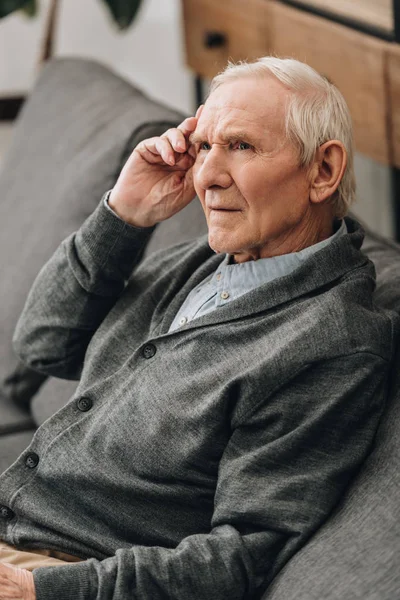 Nachdenklicher Rentner mit grauen Haaren sitzt auf Sofa — Stockfoto