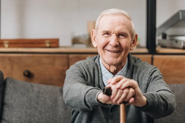 Fröhliche Rentnerin lächelt und hält Spazierstock zu Hause — Stockfoto