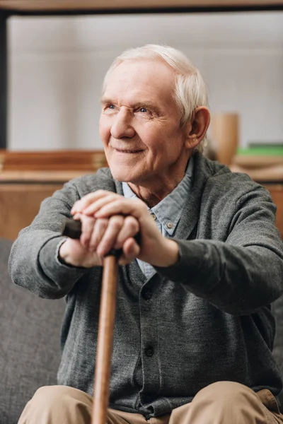 Cheerful pensioner smiling and holding walking stick at home — Stock Photo