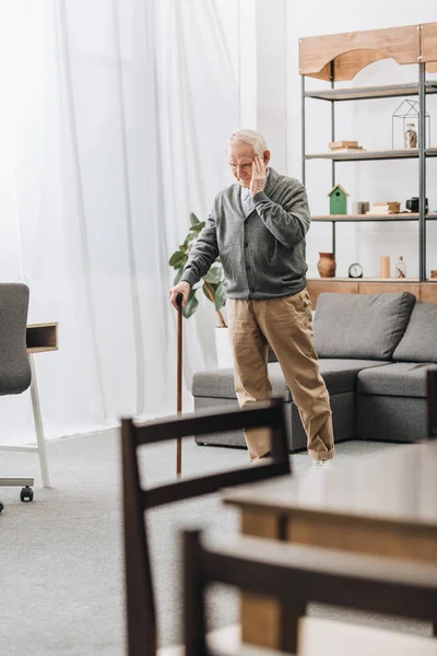 Homme à la retraite debout avec bâton de marche et ayant mal à la tête — Photo de stock