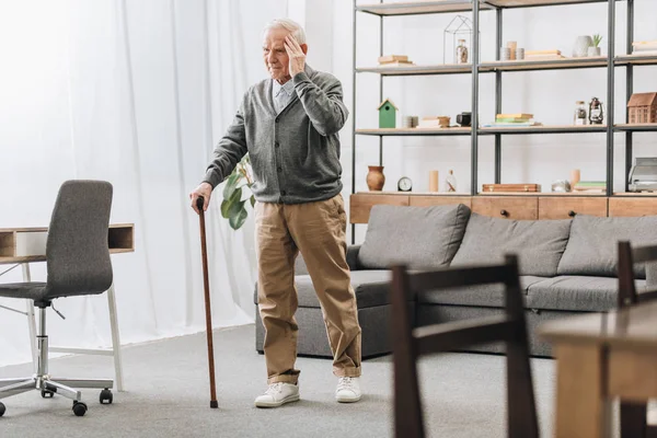 Старший чоловік стоїть з ходячою тростиною, маючи головний біль — стокове фото