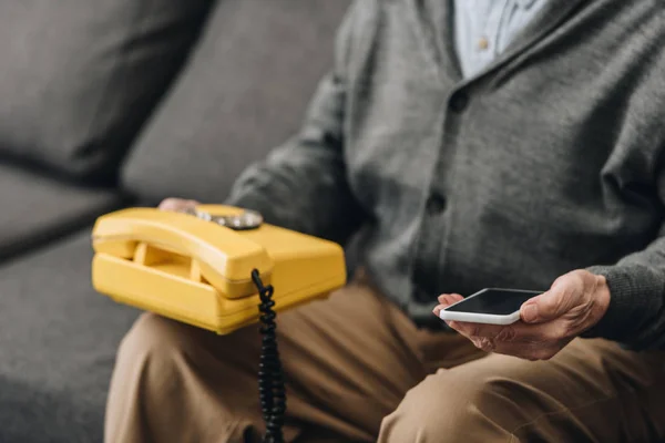 Cropped view of smartphone and old phone in hands of senior man — Stock Photo