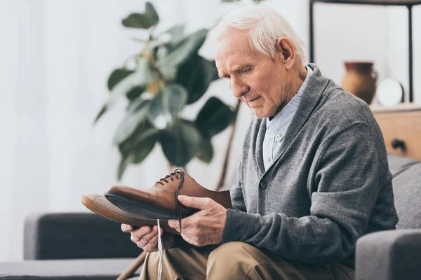 Senior man holding shoes in hands while sitting on sofa — стоковое фото