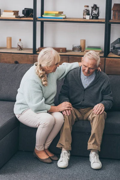 Seniorin sitzt neben Ehemann im Ruhestand und hält Händchen im Wohnzimmer — Stockfoto