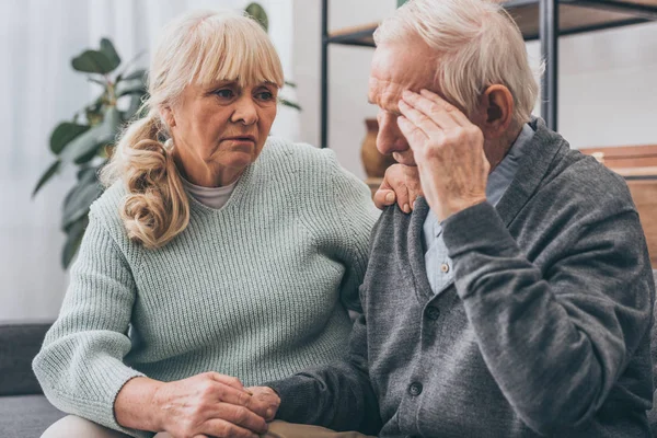 Rentnerin hält Händchen mit älterem Mann, der Kopfschmerzen hat — Stockfoto