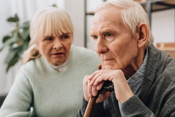 Selective focus of sad pensioner sitting near senior wife at home — Stock Photo