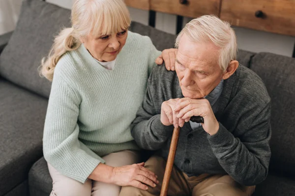 Supportive senior wife sitting near sad retired husband with walking cane — Stock Photo