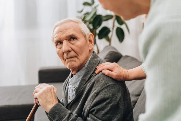 Sconvolto marito in pensione seduto in soggiorno e guardando la moglie anziana — Foto stock