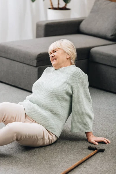 Retired woman with blonde hair sitting on floor and having pain — Stock Photo