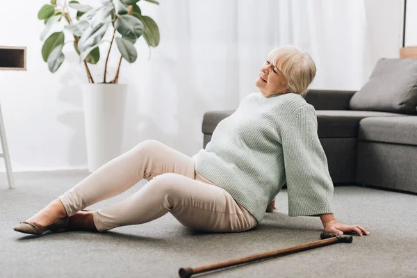 Senior woman with blonde hair sitting on floor near sofa — Stock Photo