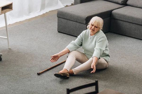 Hilflose Seniorin mit blonden Haaren sitzt auf dem Boden neben Sofa — Stockfoto