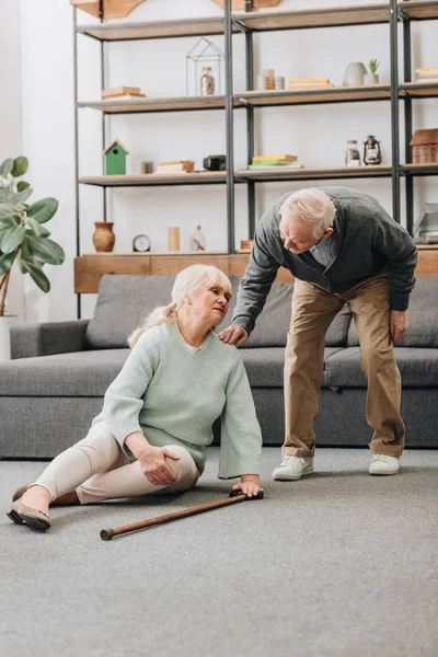Seniorin sitzt mit Schmerzen im Knie neben Rentner-Mann auf dem Boden — Stockfoto