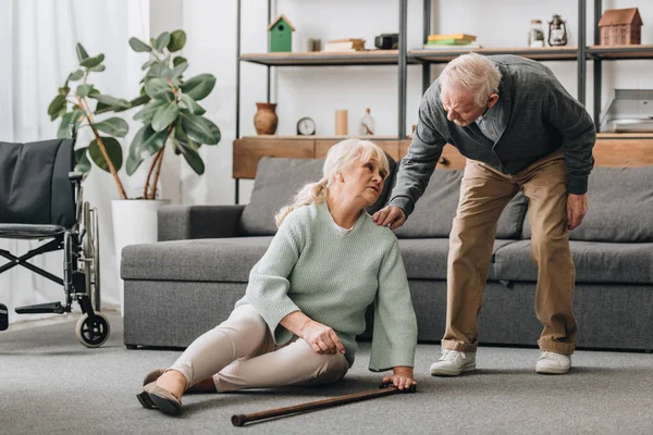 Senior wife sitting on floor with pain in knee near supportive retired husband — Stock Photo