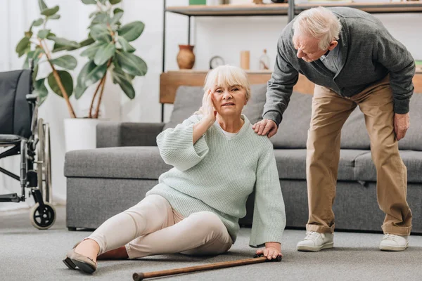 Senior wife sitting on floor with headache near supportive retired husband — Stock Photo