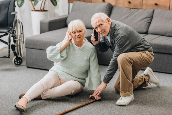 Старшая жена сидит на полу, пока муж на пенсии разговаривает по смартфону — стоковое фото