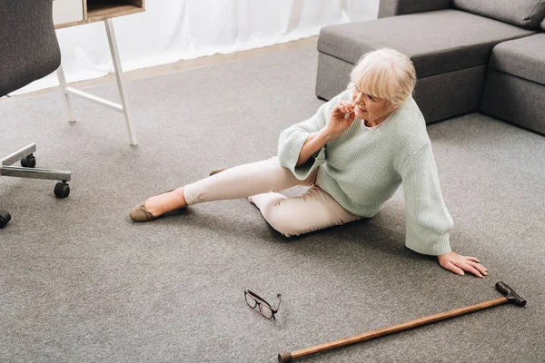 Femme âgée solitaire avec des cheveux blonds assis sur le sol dans le salon — Photo de stock