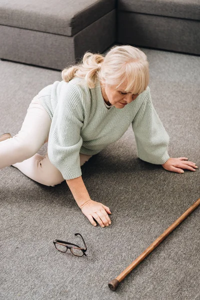 Mujer mayor indefensa con el pelo rubio sentado en el suelo en casa - foto de stock
