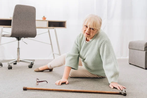 Helpless retired woman with blonde hair sitting on floor at home — Stock Photo