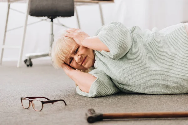 Femme retraitée sans défense couchée sur le sol dans le salon tout en ayant mal à la tête — Photo de stock