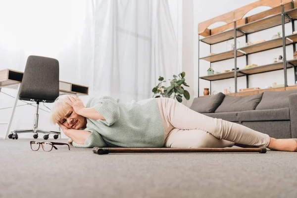 Femme retraitée solitaire couchée sur le sol dans le salon et tenant la tête — Photo de stock