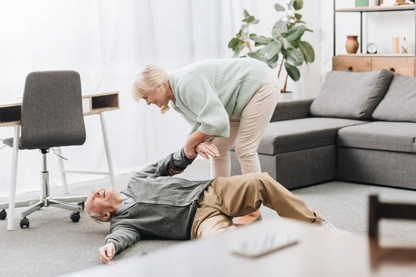 Old woman helping to husband who falled down on floor — Stock Photo