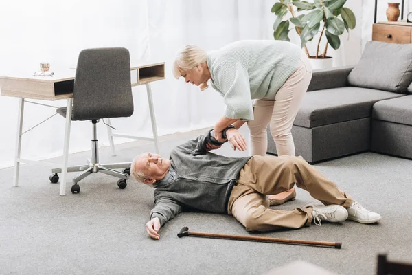 Пожилая женщина помогает мужу, который упал от сердечного приступа — стоковое фото