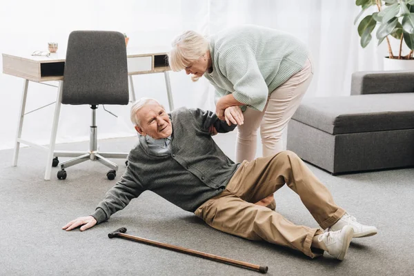 Old woman helping to stand up husband who falled down on floor — Stock Photo