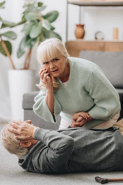 Senior woman helping old man with walking stick and looking at camera — Stock Photo