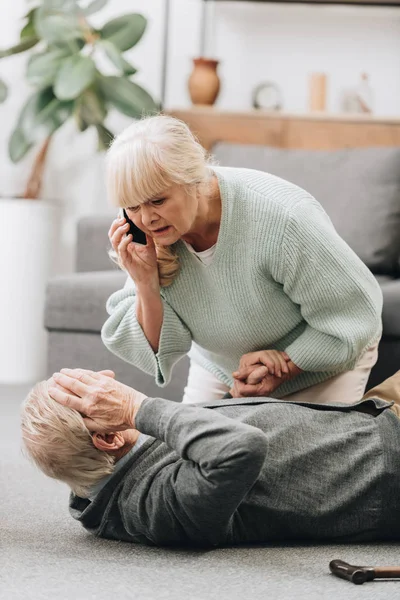 Senior woman helping to husband who falled down on floor and holding hand — Stock Photo