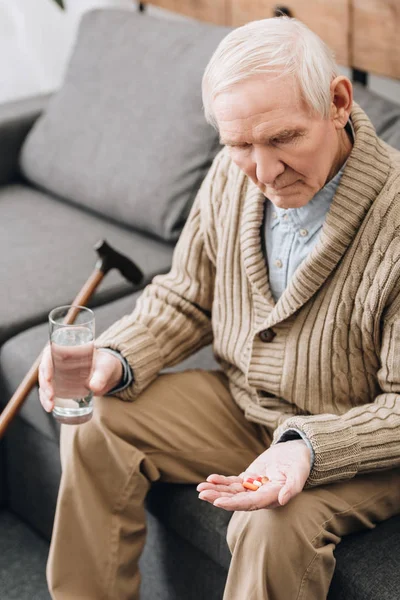 Senior hält Tabletten und Glas Wasser in der Hand und schaut auf die Hand — Stockfoto