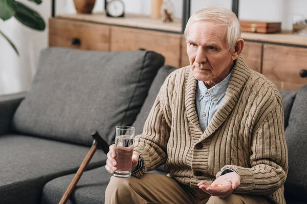 Senior man with walking stick holding pills and glass of water — Stock Photo