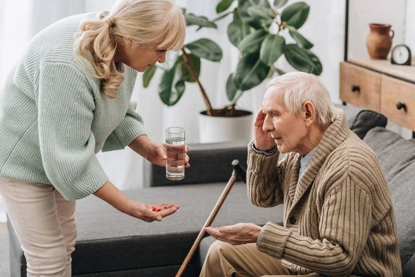 Старша жінка дає таблетки старому чоловікові з ходьбою палицею — стокове фото