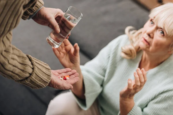 Old woman taking glass of water and pills from old man — Stock Photo