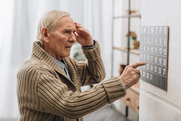 Old man looking at calendar and touching head — Stock Photo