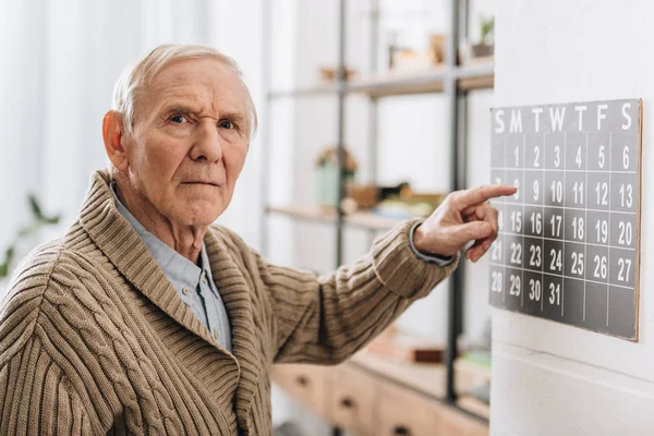 Old man touching calendar looking at camera — Stock Photo