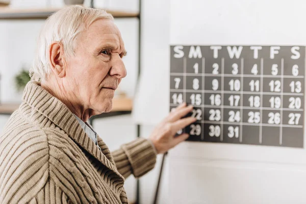 Selective focus of senior man touching wall calendar and remembering dates — Stock Photo