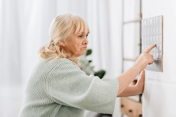 Verärgerte Seniorin berührt Wandkalender und erinnert sich an Daten — Stockfoto