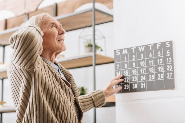 Homem sênior tocando calendário de parede e cabeça — Fotografia de Stock